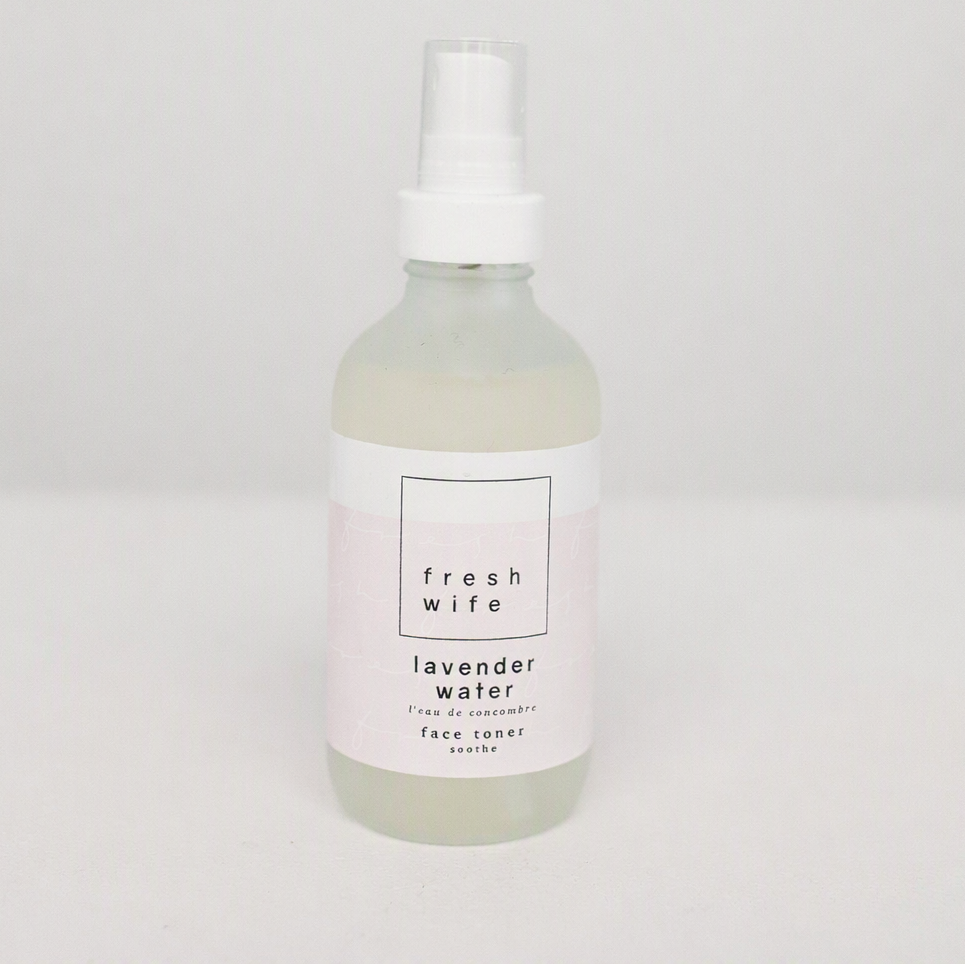 A frosted glass spray bottle of Fresh Wife Lavender Water face toner with a white label and white spray cap, set against a plain light gray background.